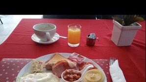A breakfast plate with eggs, bacon, toast, beans, and a glass of orange juice on a red tablecloth. - Bua Khao Paradise (Pattaya)