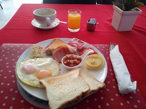 A breakfast plate with eggs, bacon, toast, beans, and a glass of orange juice on a red tablecloth. - Bua Khao Paradise (Pattaya)