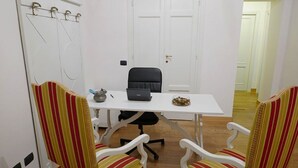 A small office with a white desk, black office chair, and striped chairs. There is a laptop, a small bowl, and a pen on the desk. - Residenza Maiano (Florence)