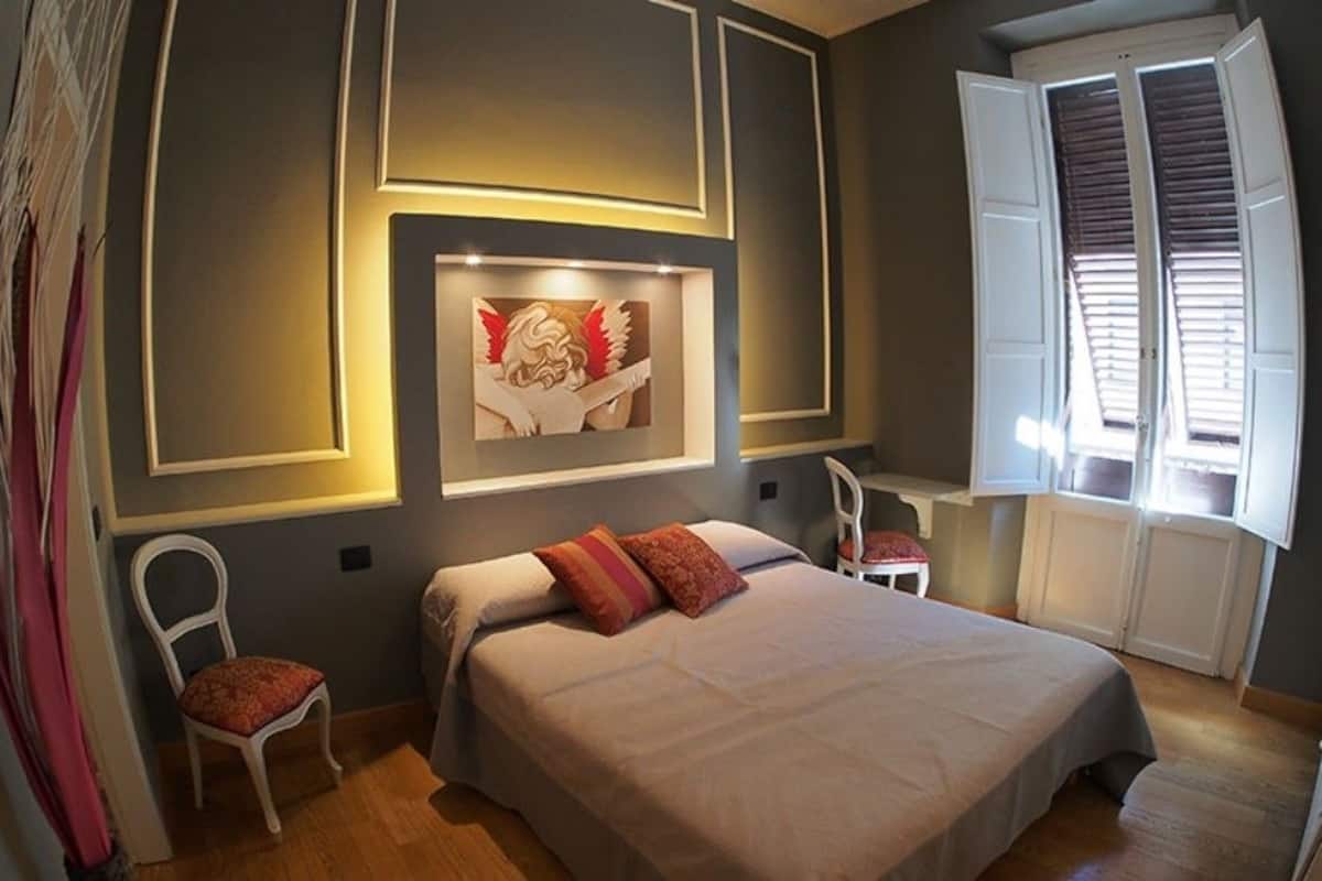 A bedroom with a bed, a chair, a desk, and a window with blinds.