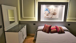 Een slaapkamer met een bed, een ladekast, een spiegel en een lijst met een kunstwerk aan de muur.