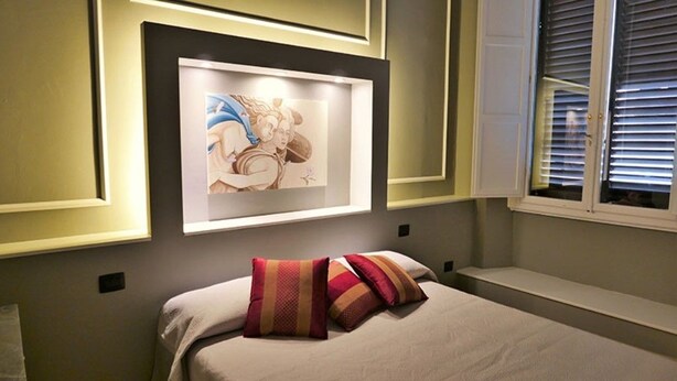 A bedroom with a bed, pillows, a framed artwork on the wall, and a window with blinds. - Residenza Maiano (Florence)