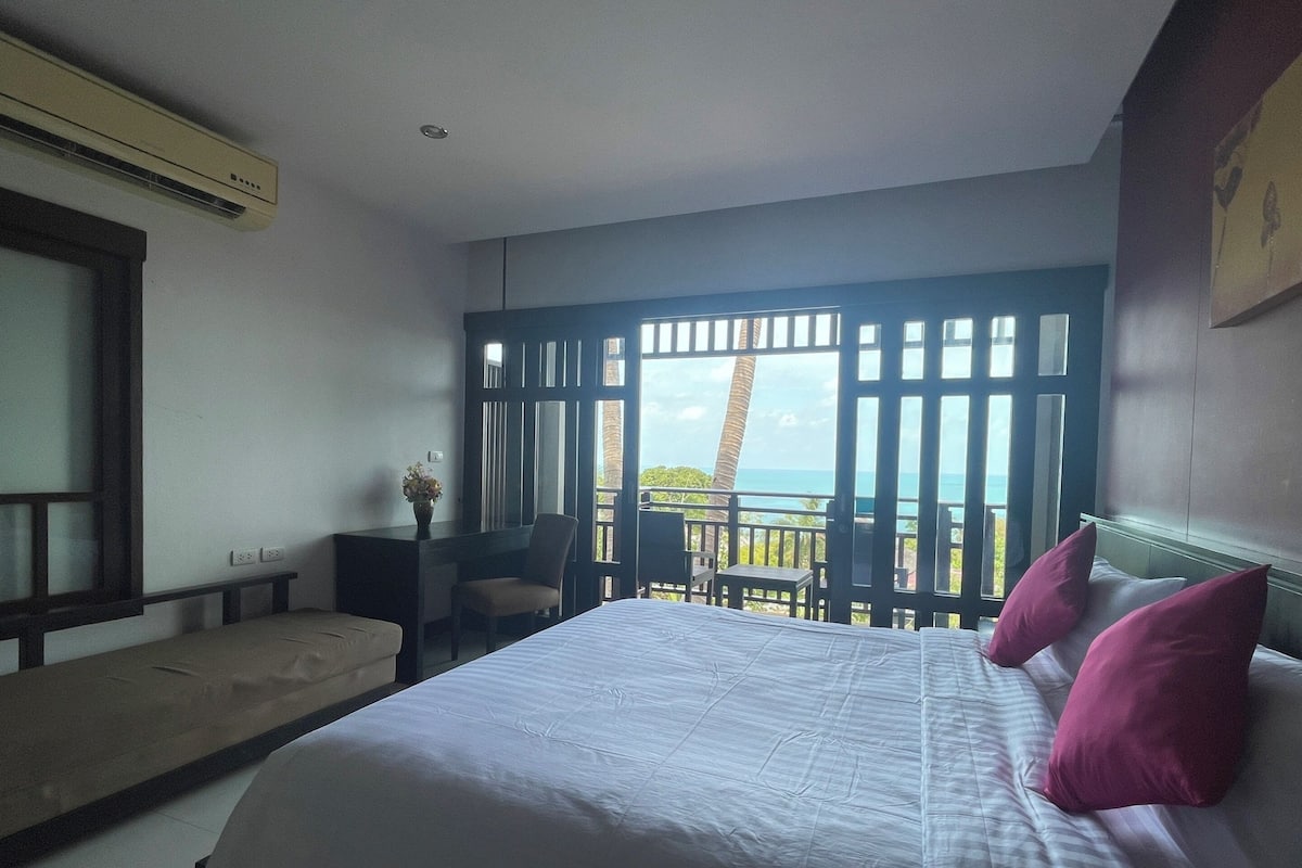 A bedroom with a bed, a desk, and a view of the ocean.