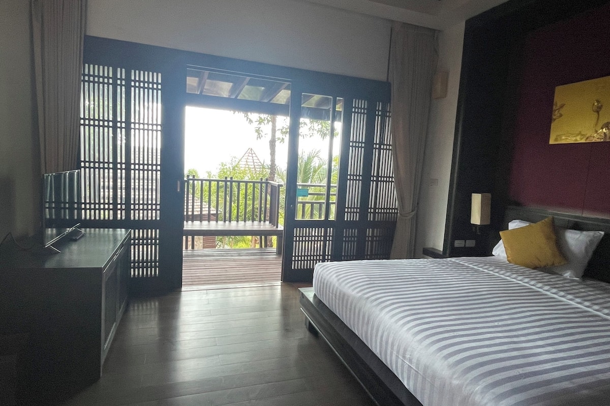 A hotel room with a bed, a desk, and a balcony with a view.