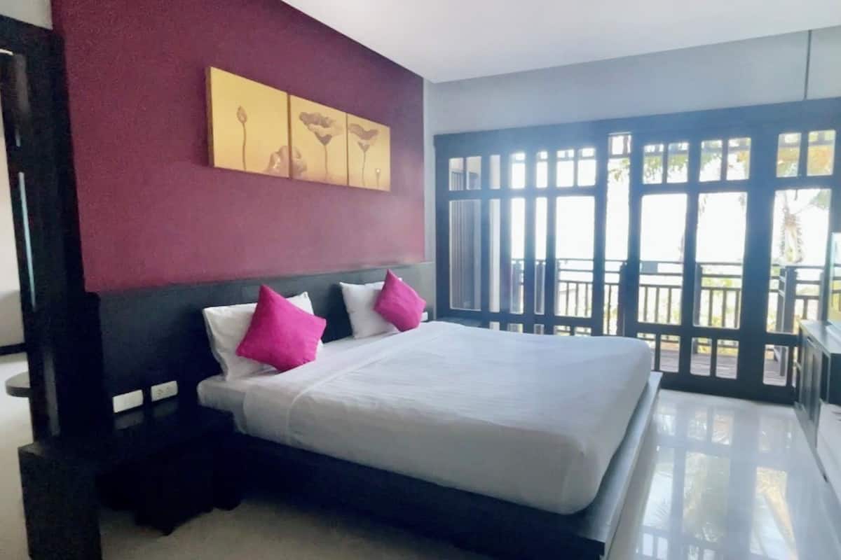 A bedroom with a bed, a nightstand, a window with a view, and artwork on the wall.