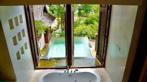 A bathroom with a bathtub, a window overlooking a pool and garden. - Bhundhari Residence Koh Samui (Koh Samui)
