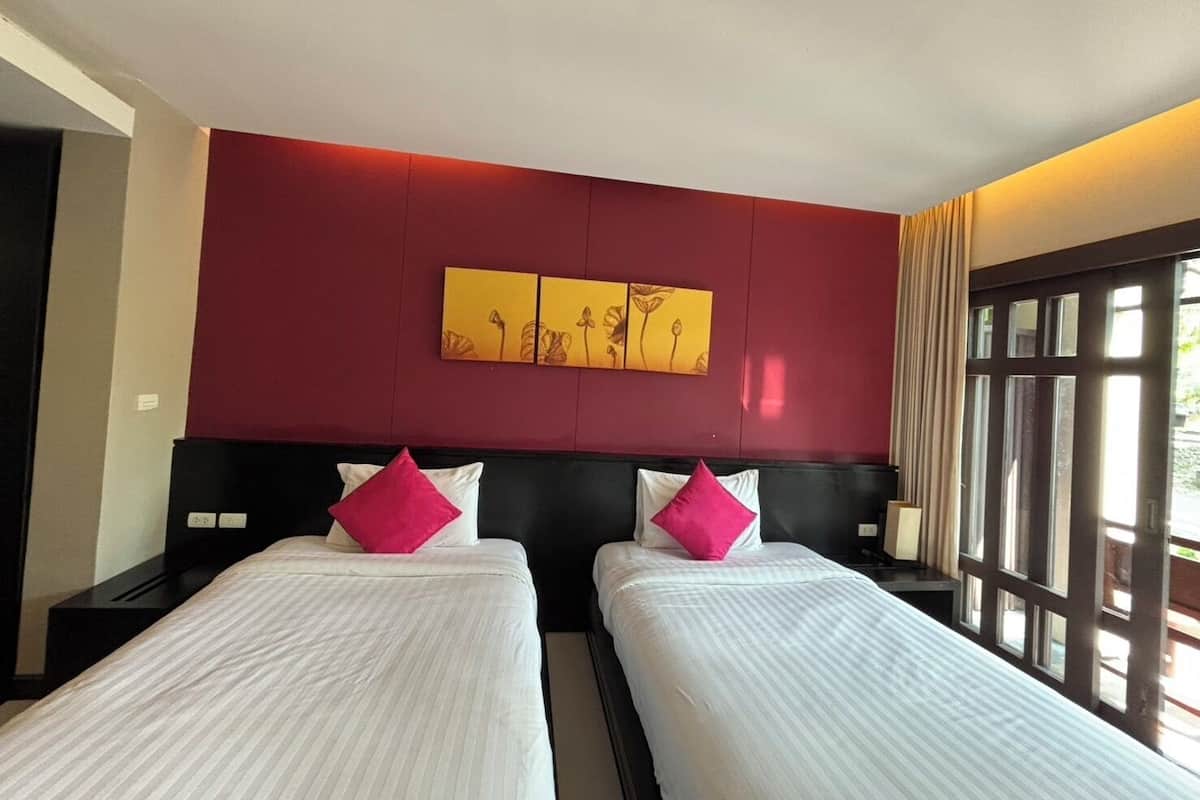 A hotel room with two beds, a red accent wall, and a large window.