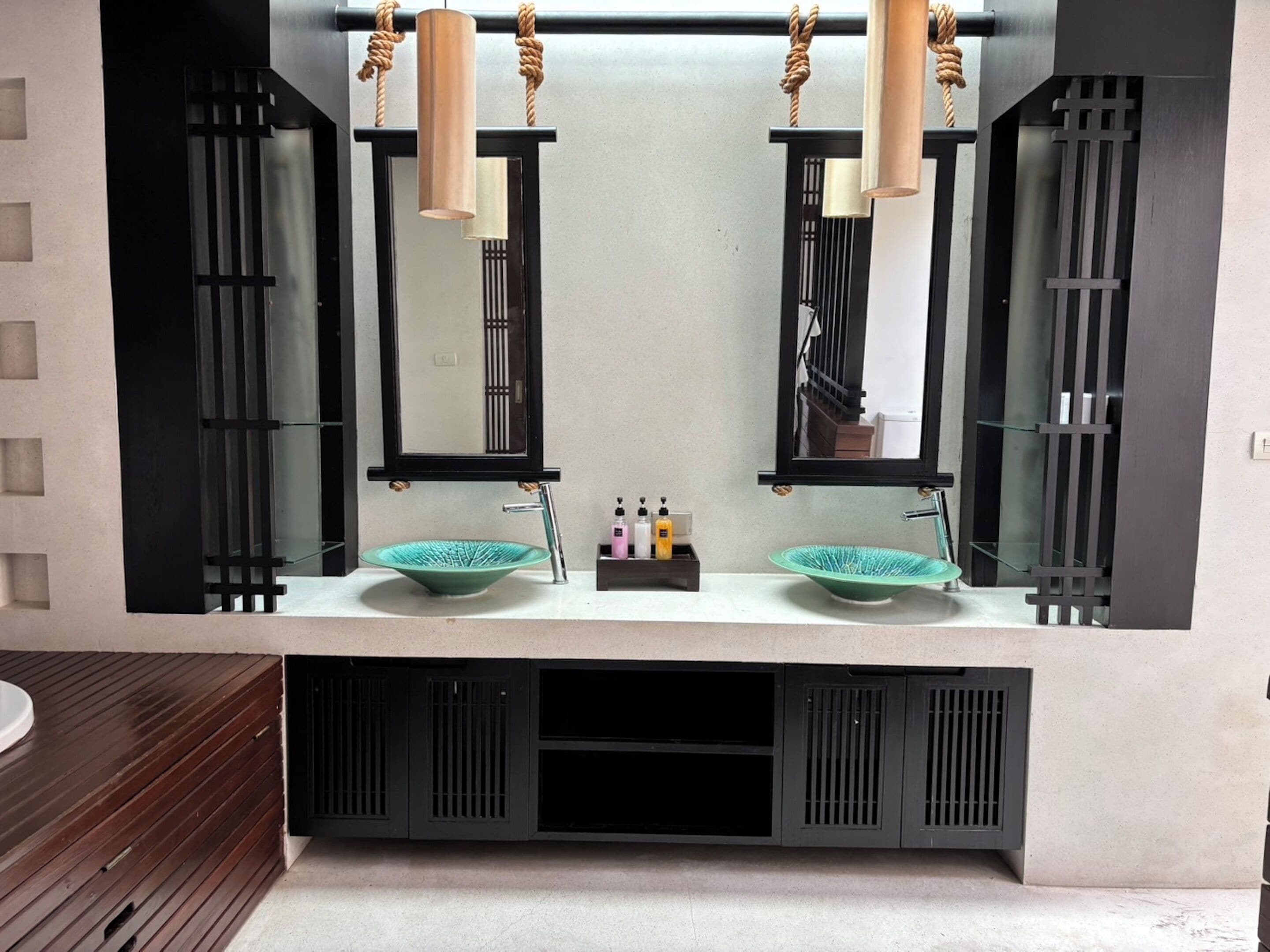 Une salle de bain au design moderne, dotée d’un double lavabo avec un récipient vert, d’un grand miroir et d’un meuble-lavabo en bois.