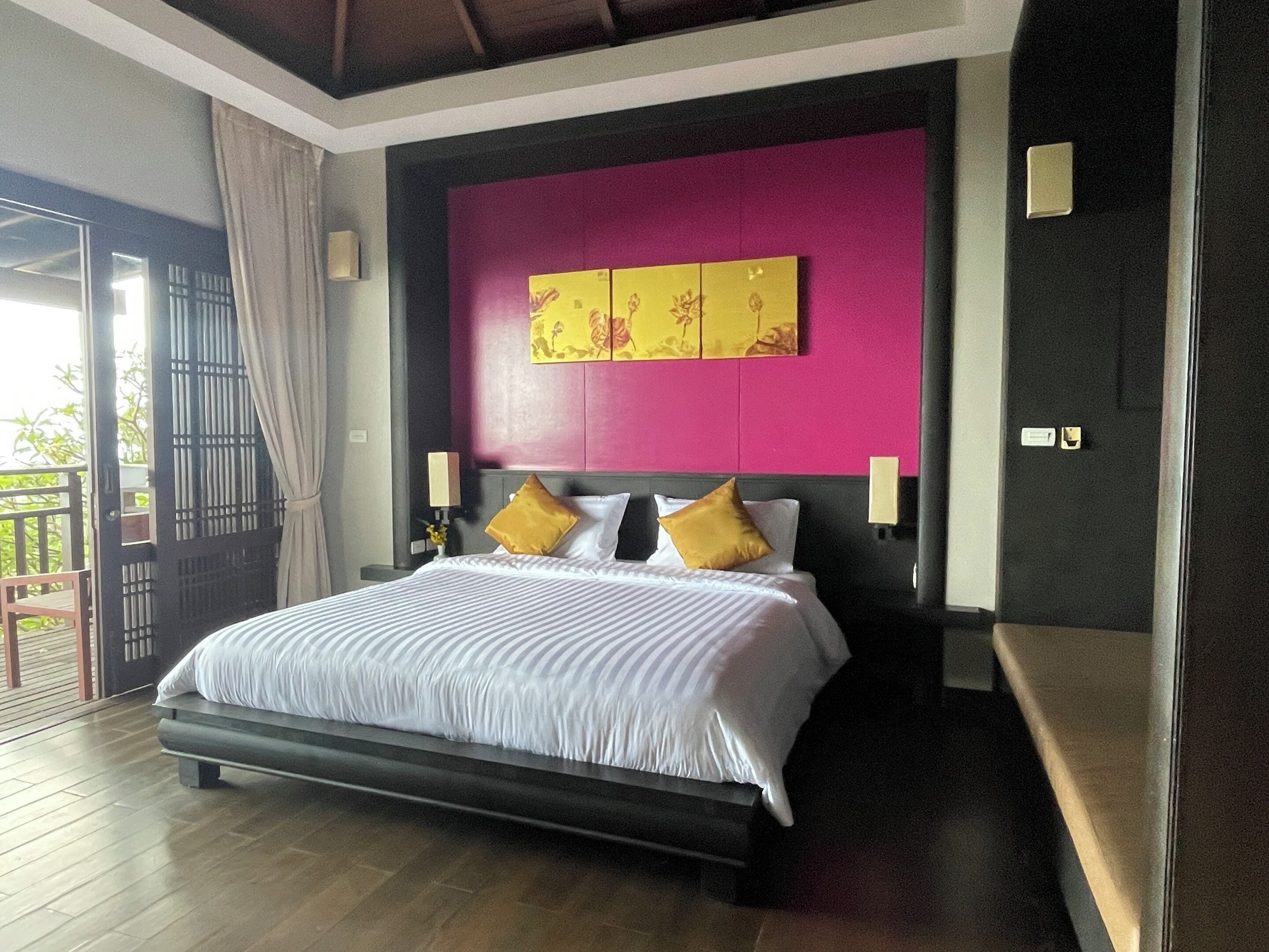 Une chambre d’hôtel avec un grand lit, une vue sur l’extérieur et un mur d’accent d’un rose vif.