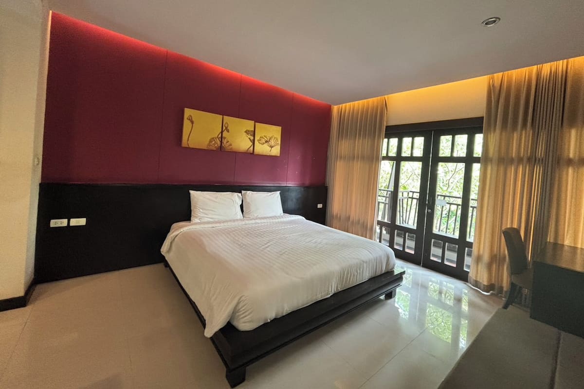 A modern bedroom with a large bed, a red accent wall, and a window with curtains.