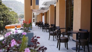 Un espacio al aire libre con mesas y sillas, vistas al paisaje y un edificio con grandes ventanales.