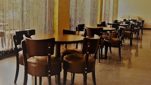 Un comedor amplio con varias mesas redondas y sillas, que cuenta con un piso reflectante y cortinas a rayas verticales.