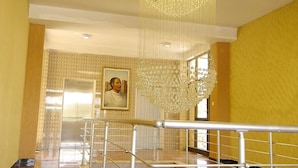 Una escalera con barandilla de metal que lleva a un rellano. Un candelabro cuelga del techo, y se ve un retrato enmarcado en la pared.