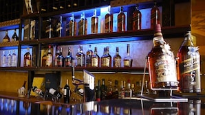 Un bar con estantes llenos de botellas de licores, un enfriador de vino y una variedad de copas de vino.