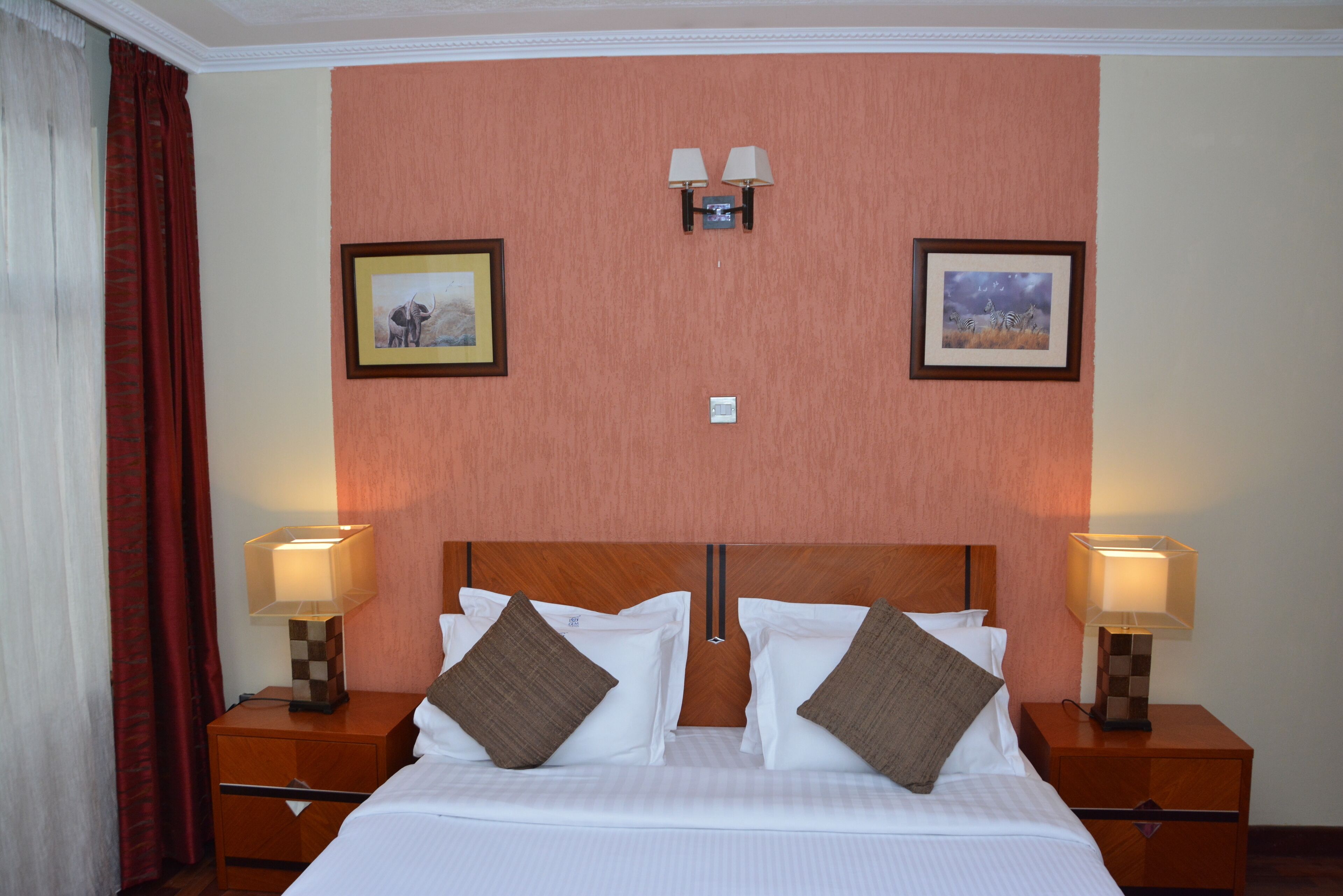 A hotel room with a large bed, two nightstands, two wall-mounted lamps, and two framed pictures on the wall.