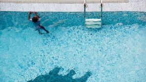 A swimming pool with a tiled floor and a person swimming.