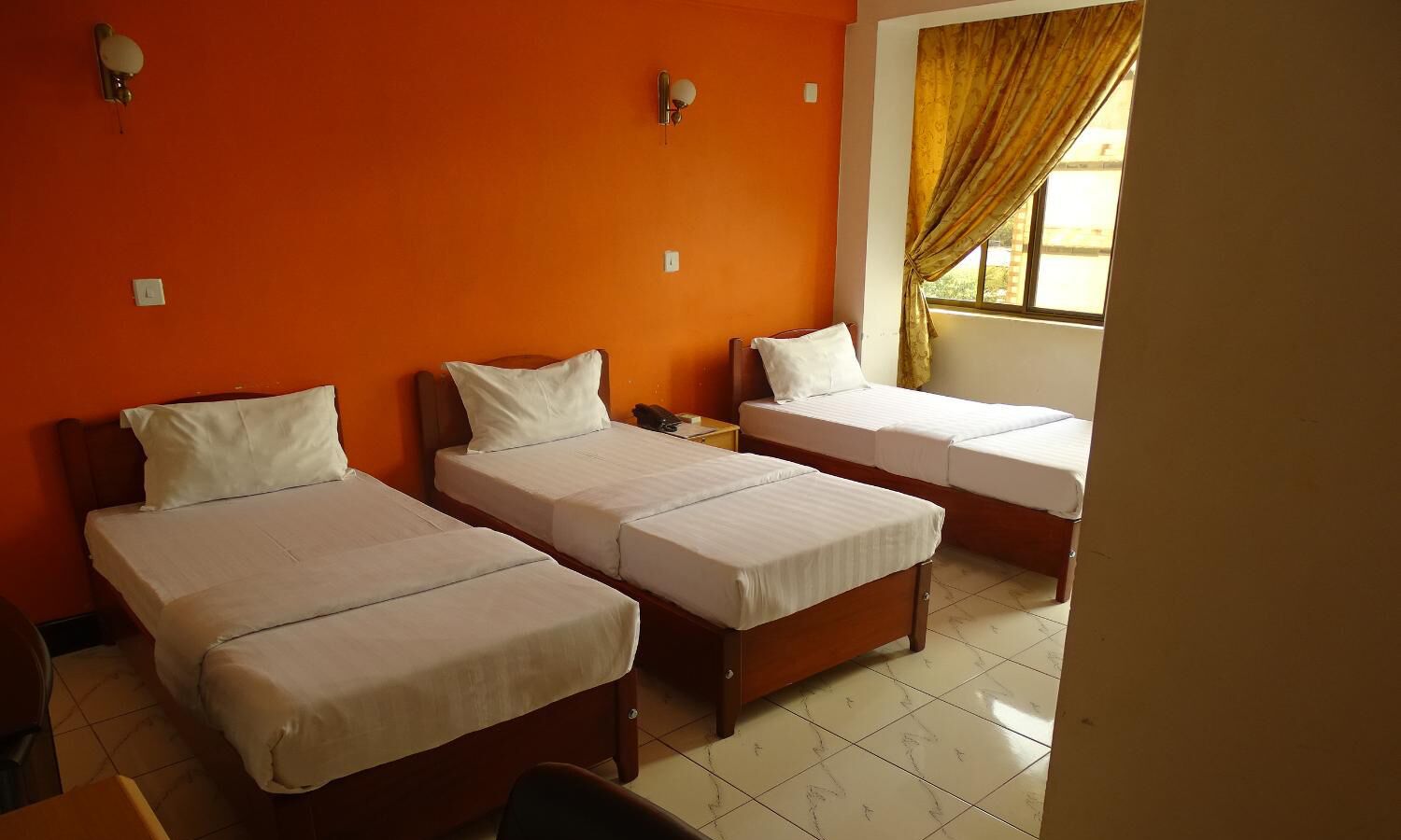 Une chambre avec trois lits simples, des murs orange et une fenêtre avec des rideaux.