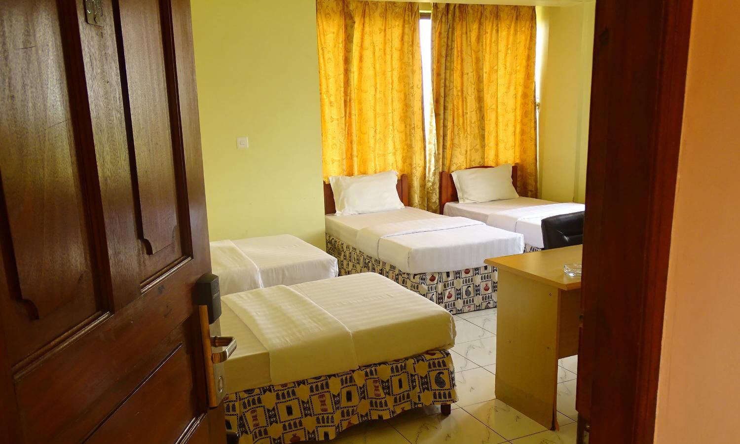 A room with two single beds, a wooden door, and a small desk with a chair.