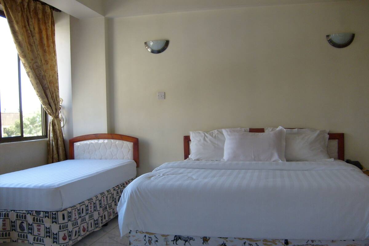 A hotel room with two beds, a window with curtains, and wall-mounted light fixtures.