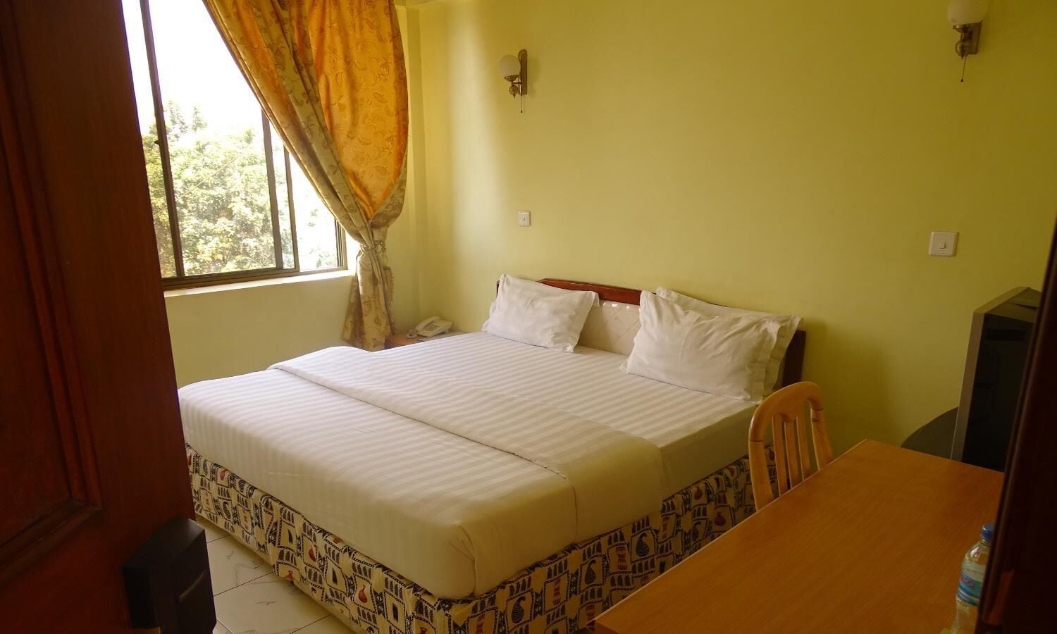 Una habitación con cama, una mesa de madera y un ventanal con cortinas.