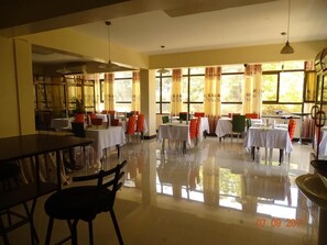 A spacious dining area with multiple tables and chairs, large windows with curtains, and a clean, reflective floor. - Panama Inn (Moshi)
