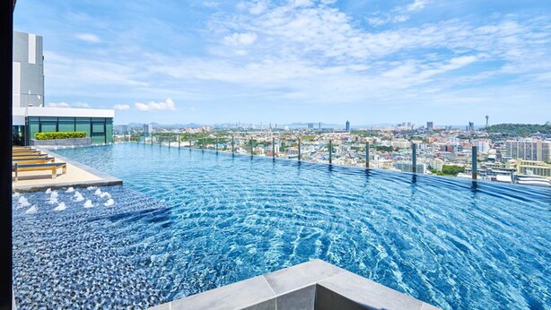 A rooftop infinity pool with a cityscape view, a modern building with a glass facade, and a clear sky. - Pattaya Central Sea View Pool Suite (Pattaya)