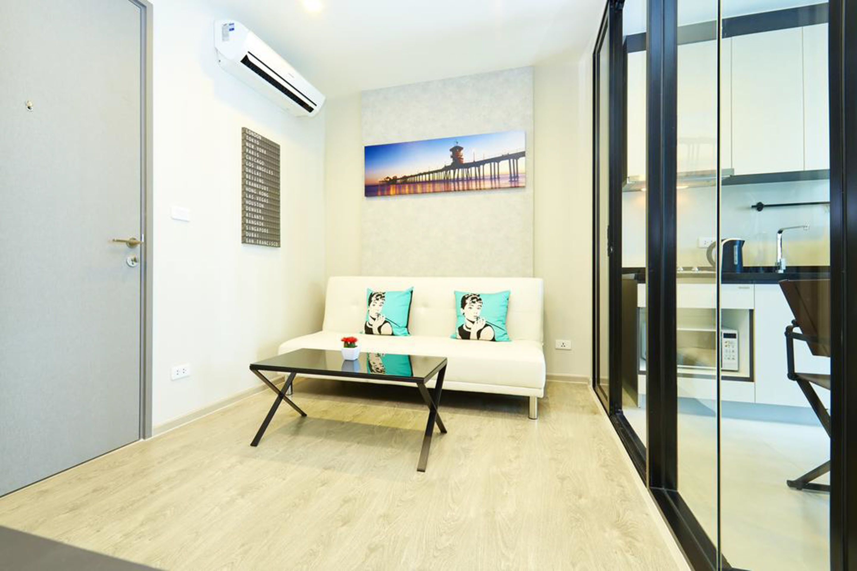 A modern living room with a sofa, a glass coffee table, and a painting of a pier.
