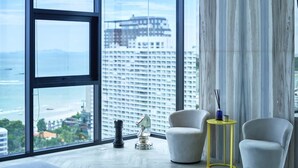 A modern living room with large windows, a view of a cityscape, and a minimalist decor. - Pattaya Central Sea View Pool Suite (Pattaya)