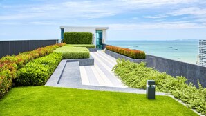 A modern building with a glass entrance, surrounded by well-maintained greenery and a view of the ocean. - Pattaya Central Sea View Pool Suite (Pattaya)
