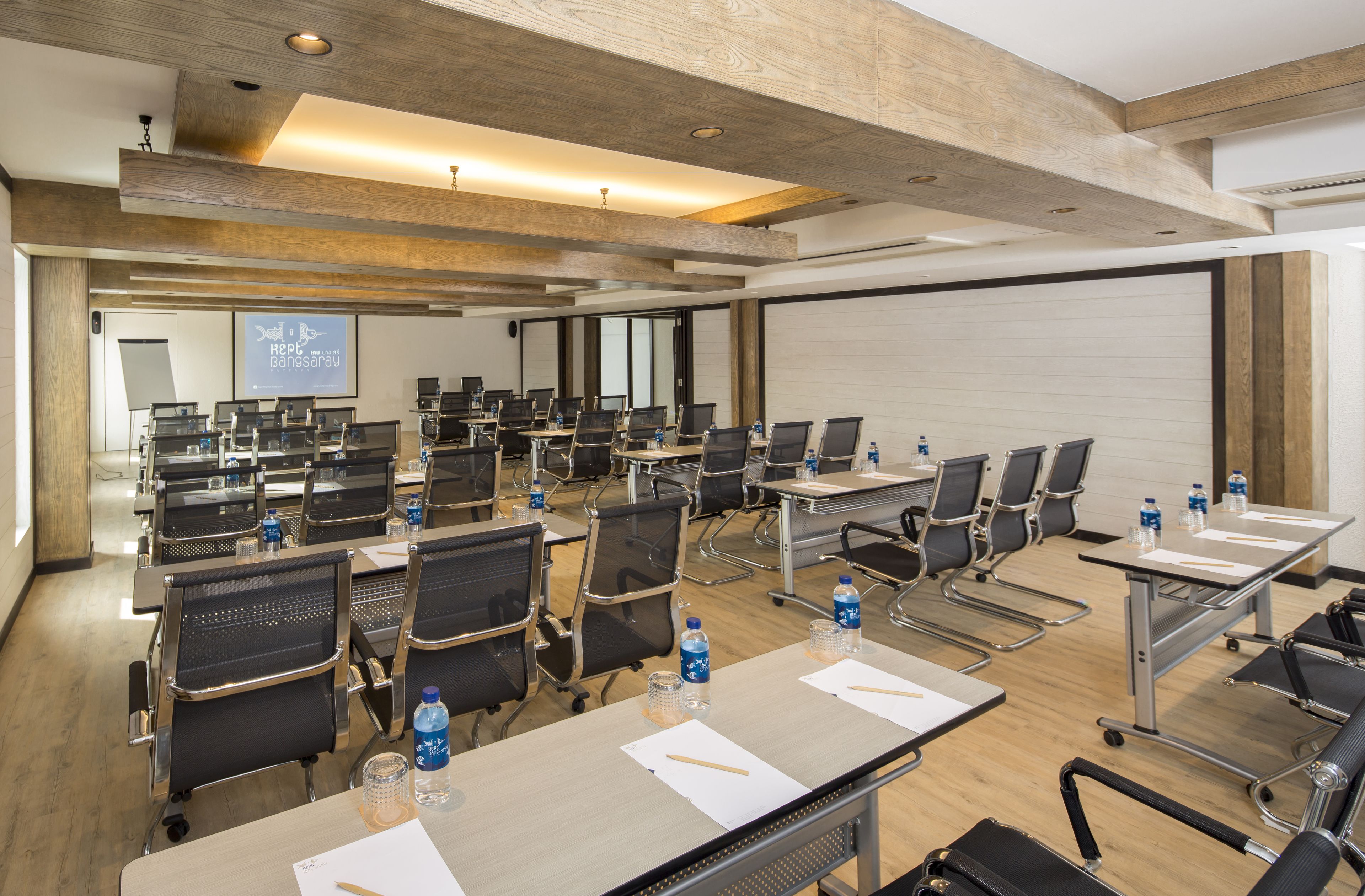 A conference room with multiple tables and chairs, equipped with laptops, water bottles, and presentation screens.