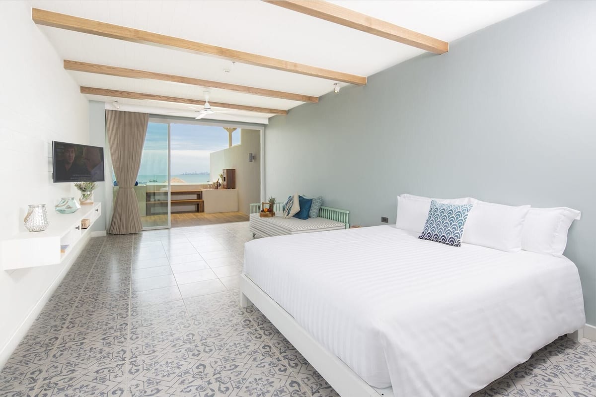 Un dormitorio con una cama grande, un televisor montado en la pared y vista al mar a través de una puerta corredera.