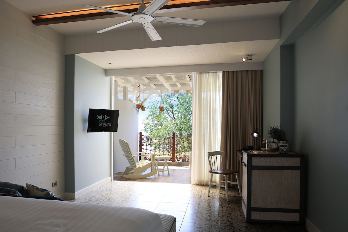 A bedroom with a bed, a desk with a lamp, a chair, and a view of an outdoor area with a swing set.
