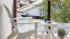 A balcony with a white chair and table, overlooking a pool area with umbrellas and lounge chairs. - Kept Bangsaray Pattaya (Sattahip)