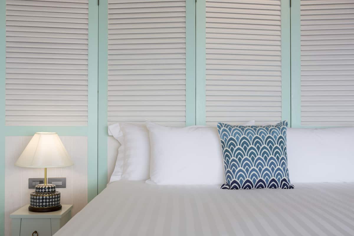 Una cama bien hecha con sábanas blancas, un cojín estampado y una mesita de noche con lámpara.