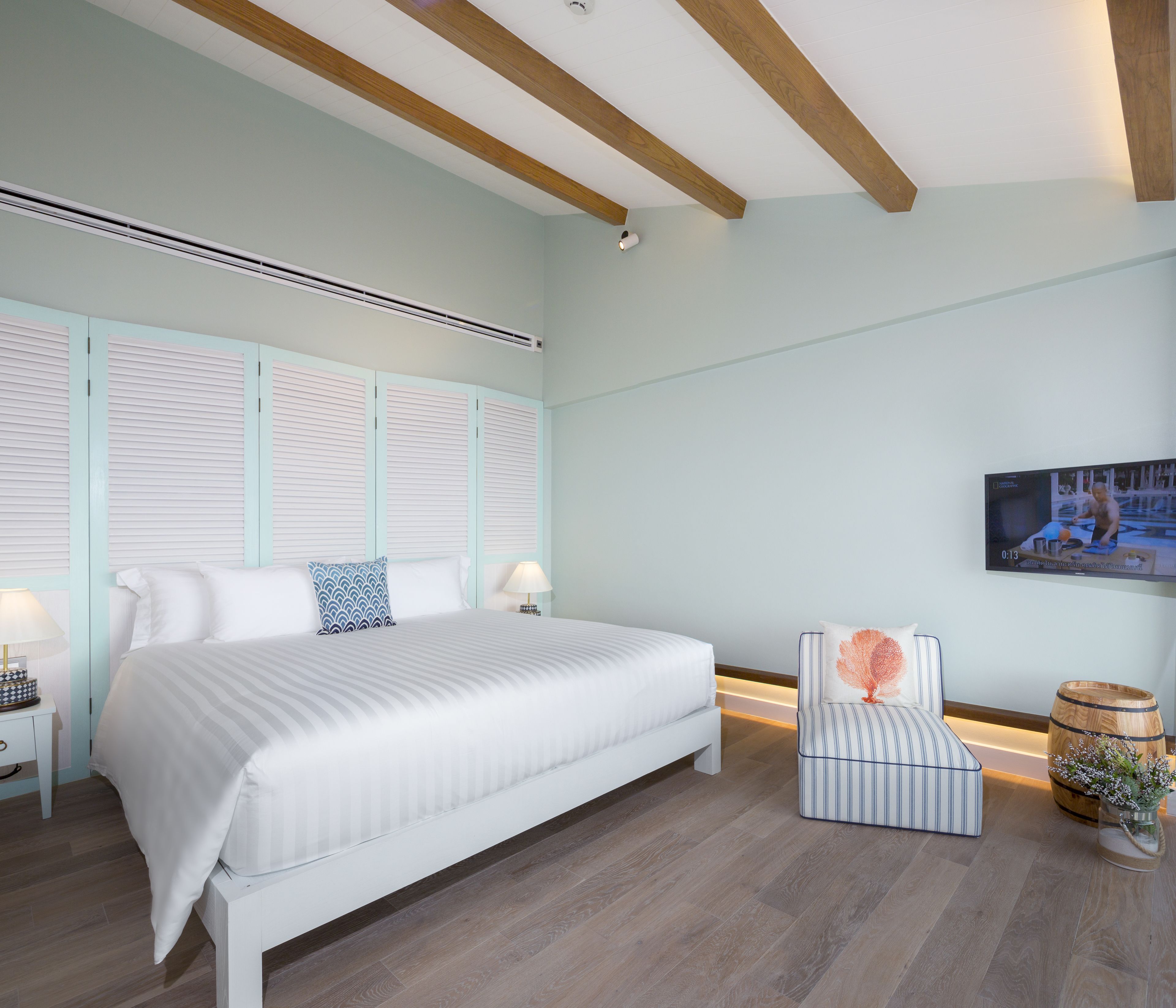 A bedroom with a large bed, a bedside table, a chair, a wooden barrel, and a wall-mounted TV.