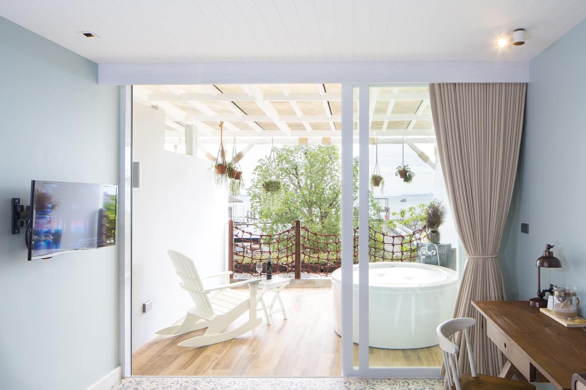 Un interior moderno con una puerta de vidrio corredera que da a un patio con hidromasaje, asientos exteriores y plantas colgantes.