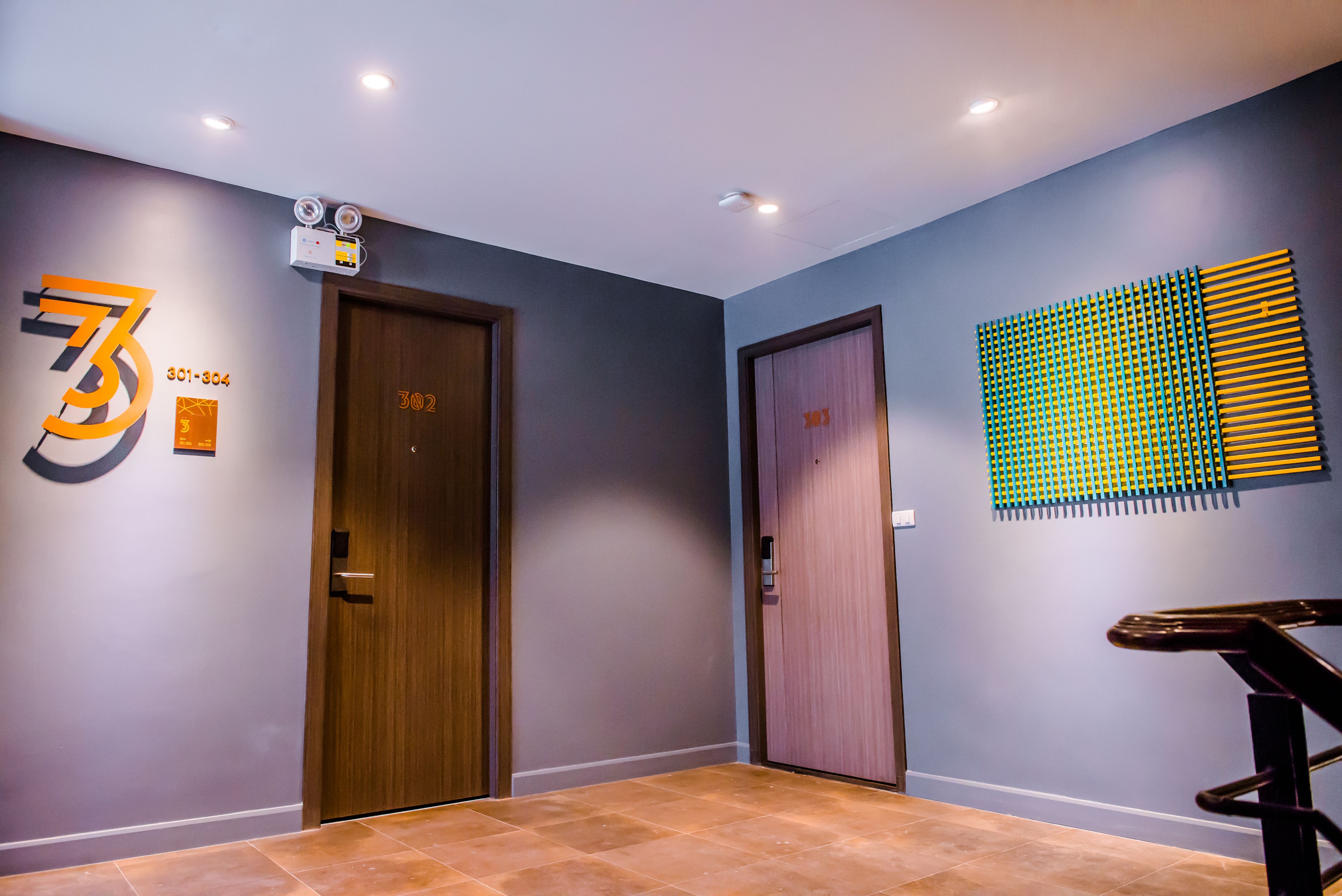 Un pasillo con dos puertas, una marcada con los números 301-304 y otra con 302-303. Hay un aplique en la pared sobre las puertas y un panel decorativo en la pared derecha.