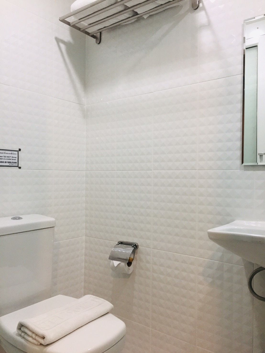 A bathroom with a toilet, a towel, a toilet paper holder, and a sink.