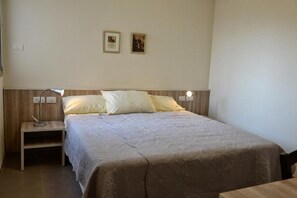 A bedroom with a bed, a nightstand, a lamp, and two framed pictures on the wall.