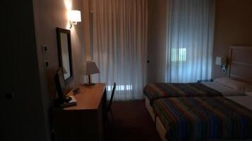 Quarto de hotel com cama, escrivaninha com cadeira, luminária e espelho.