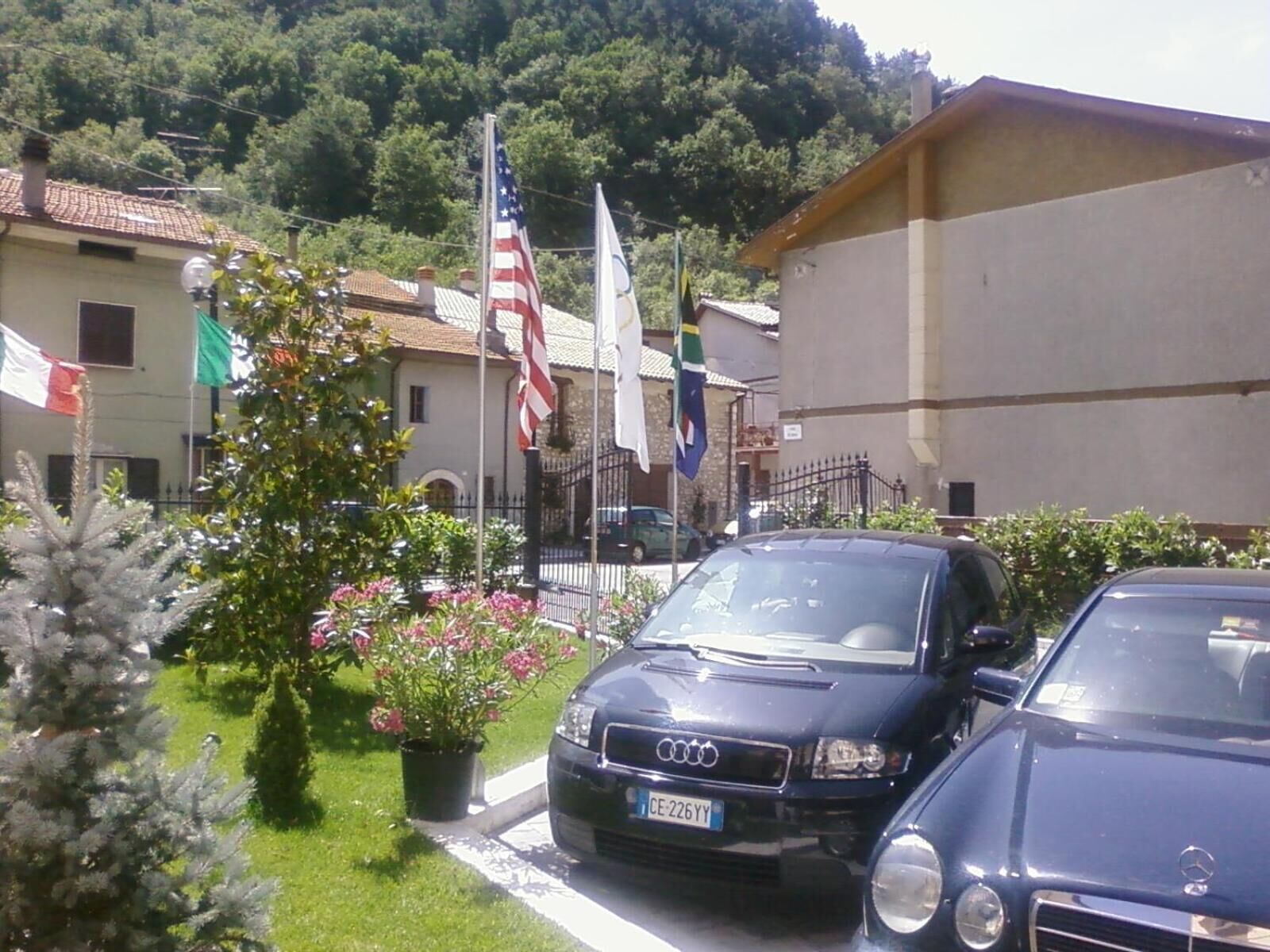 Un coche Audi estacionado en un barrio residencial, con una casa, una bandera y una planta en maceta.
