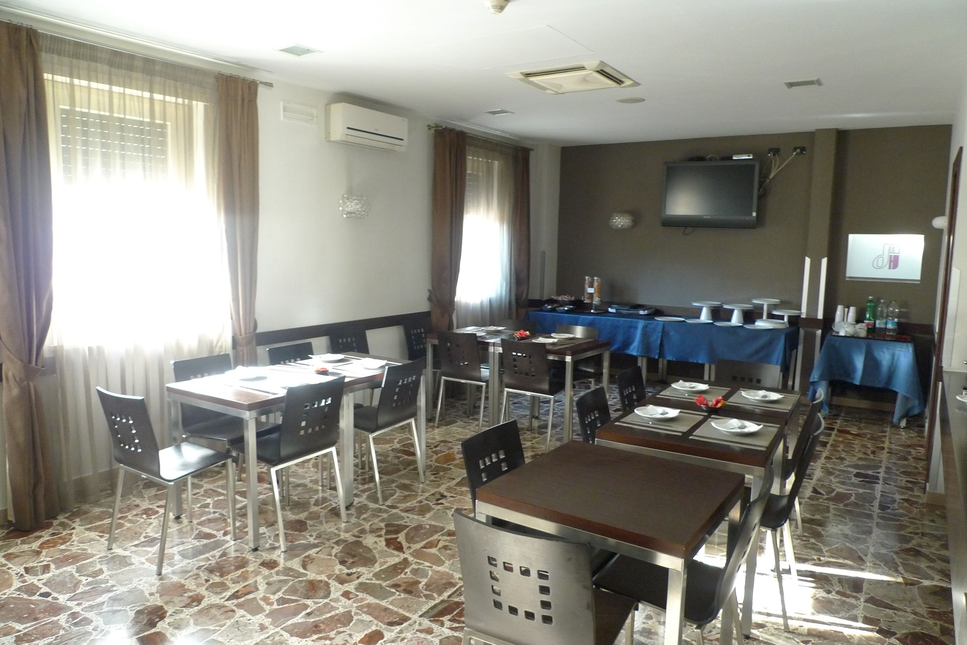 Un comedor con suelo de piedra, mesas dispuestas con sillas y un televisor montado en la pared.