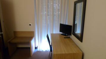 A small, dimly lit room with a wooden desk, a chair, and a television.