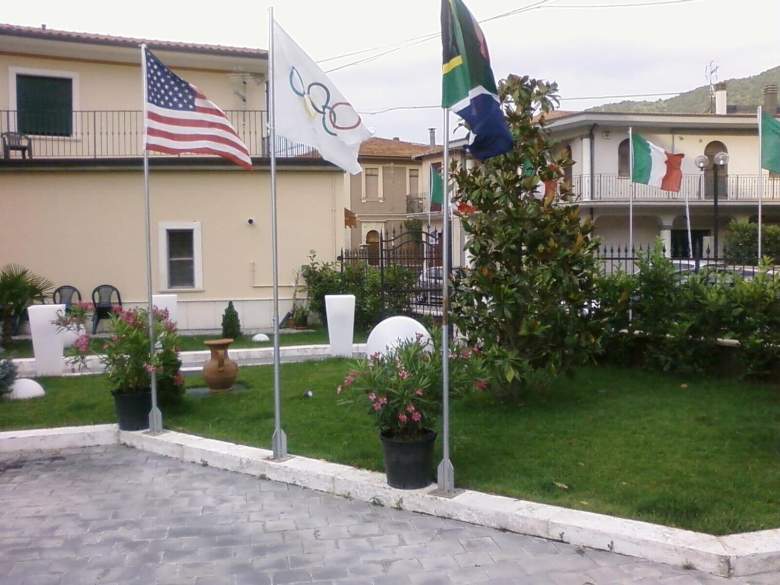 A courtyard with a paved walkway, potted plants, and flags.