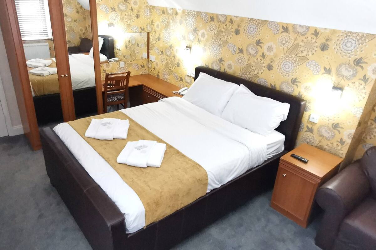A hotel room with a bed, a desk, a chair, and a wardrobe.