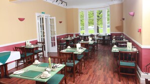 A dining area with multiple tables and chairs, a door, and windows with a view of greenery outside. - Russell Hotel (Royal Tunbridge Wells)
