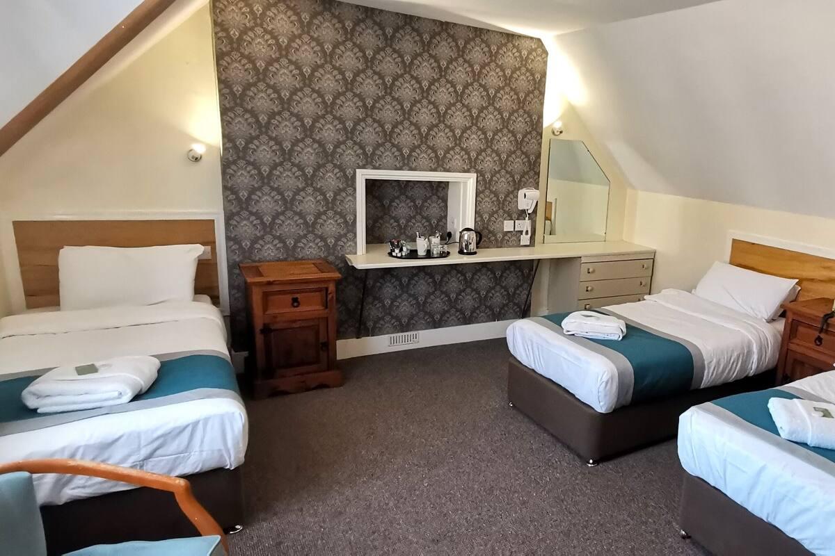 A hotel room with two single beds, a small desk, a mirror, and a patterned wallpaper.