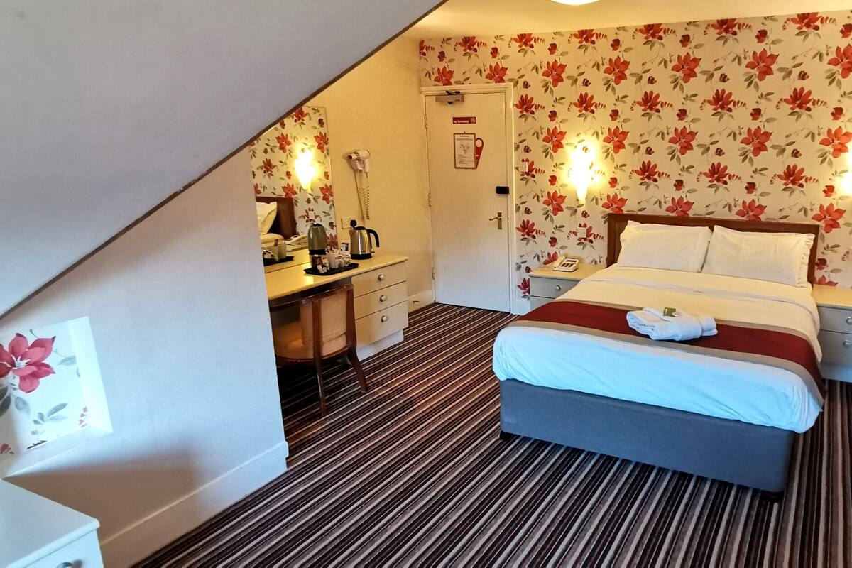 A hotel room with a bed, bedside table, desk, chair, and a mirror.
