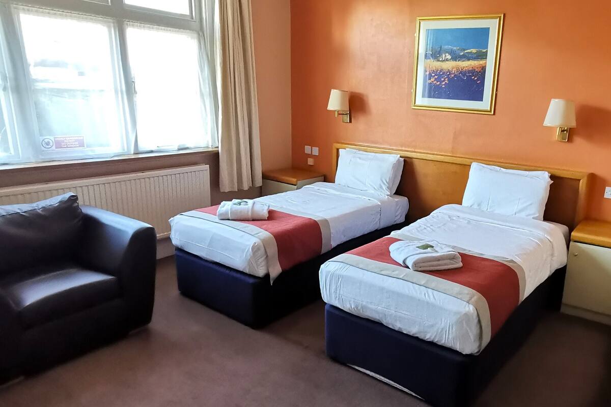 A hotel room with two beds, a sofa, and a window with curtains.
