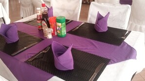 A table set with purple napkins, black placemats, and condiments. - Samanene Beach Hotel (Mwanza)